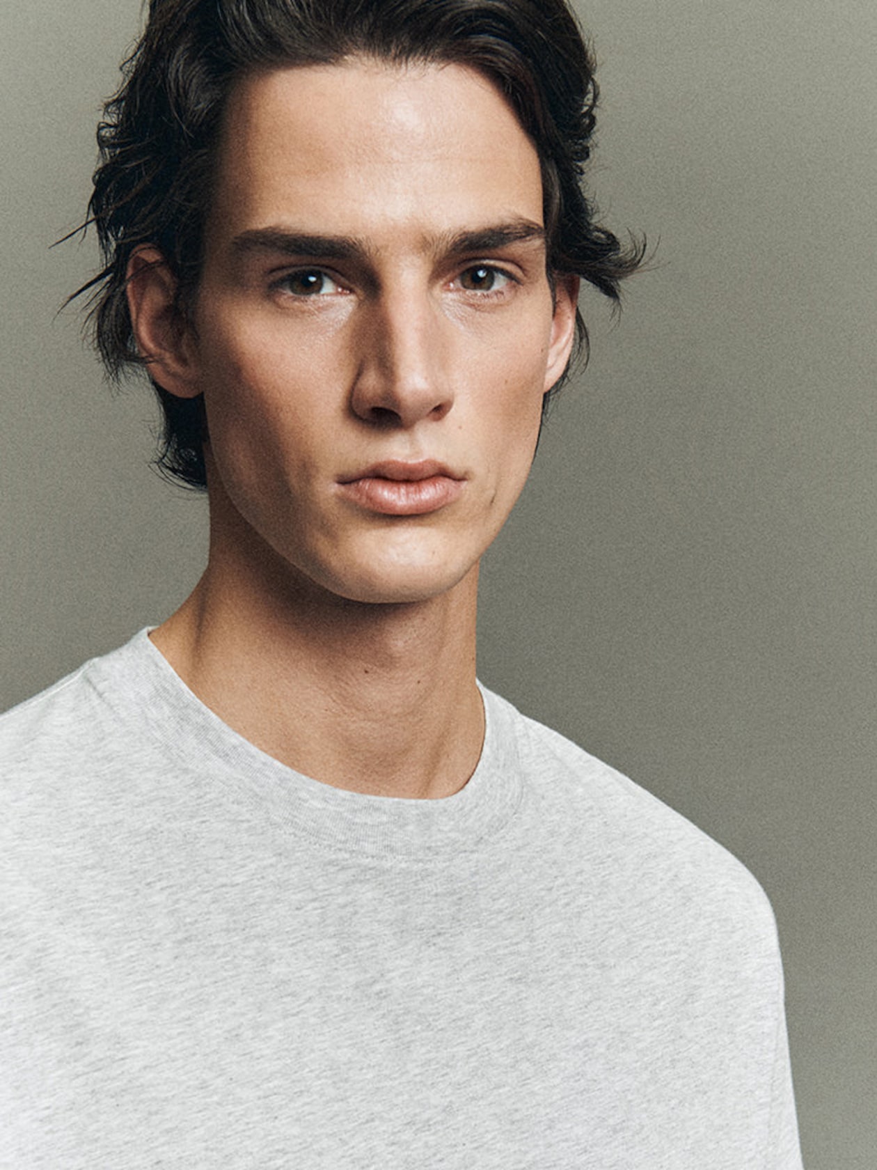 Young man with brown hair wearing a gray t-shirt, looking confidently at the camera against a neutral background.