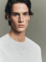 Placeholder for: Young man with brown hair wearing a gray t-shirt, looking confidently at the camera against a neutral background.