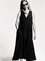 Placeholder for: A woman wearing sunglasses and a long, sleeveless black dress poses confidently in a monochrome setting.