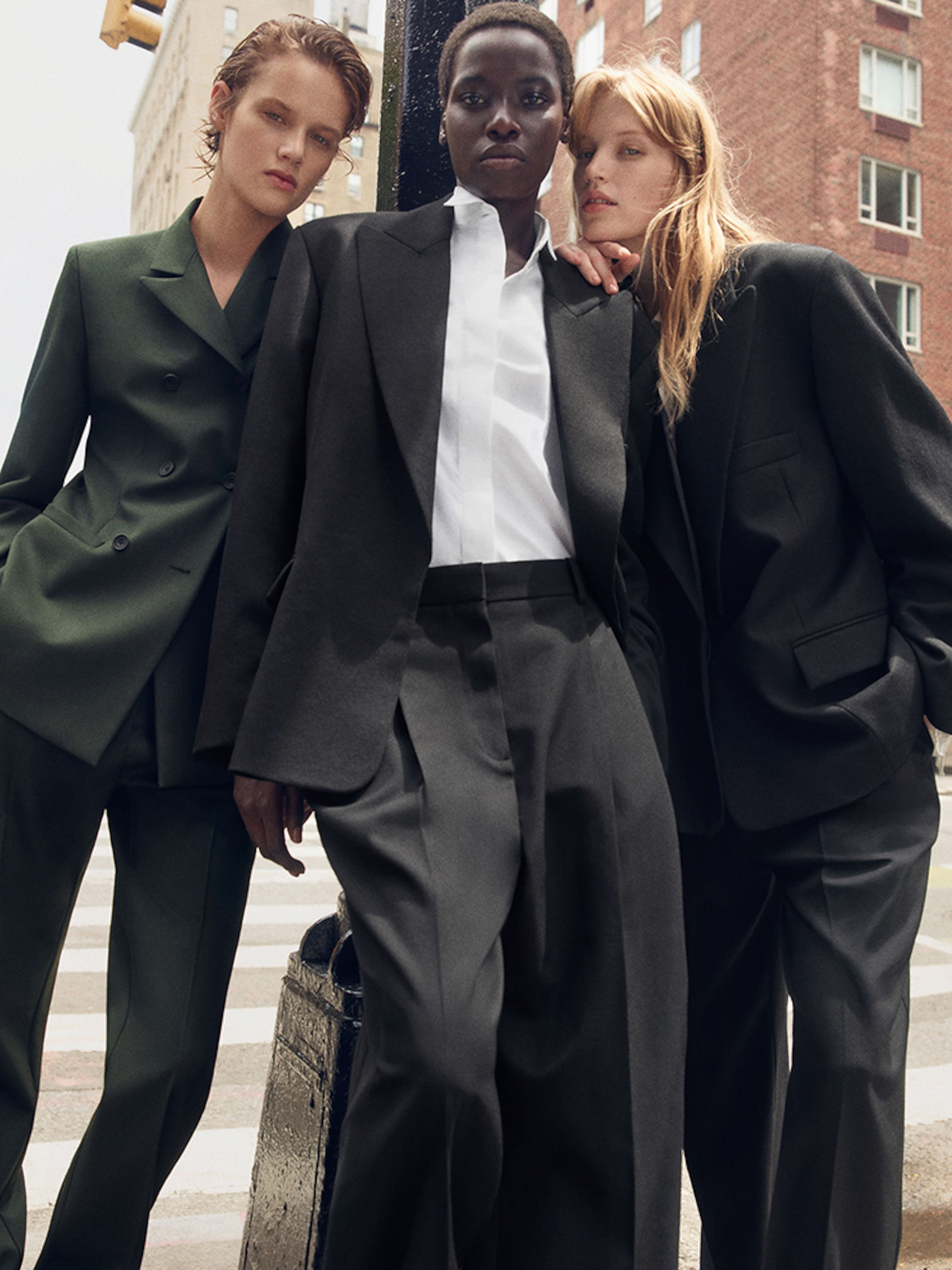 Three individuals pose in stylish, oversized suits on a city street, exuding confidence and modern sophistication.