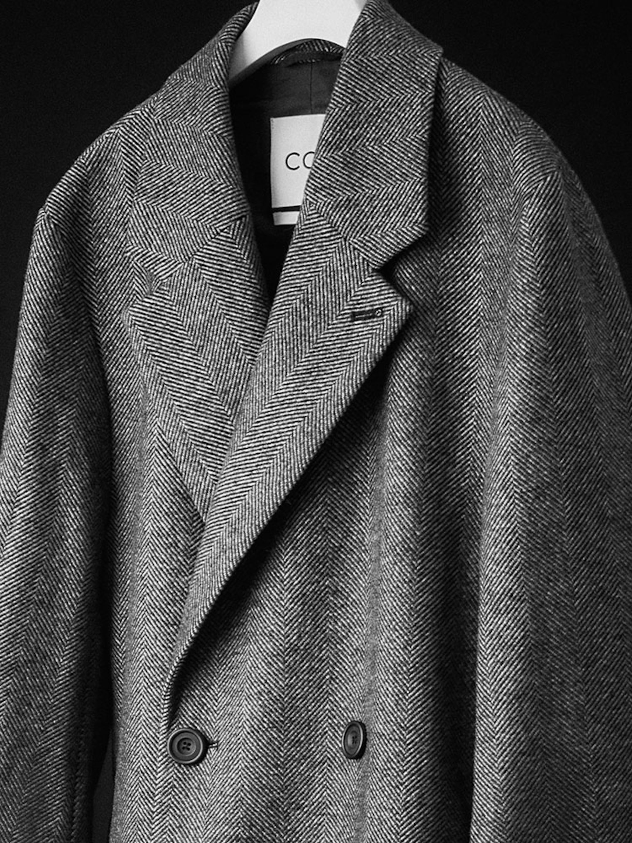 Black and white image of a herringbone coat hanging