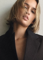 Placeholder for: Person with short blonde hair wearing an oversized black blazer, standing against a plain background.