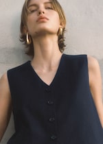 Placeholder for: Model leaning against the wall. She's wearing golden hoop earrings and is wearing a black top.