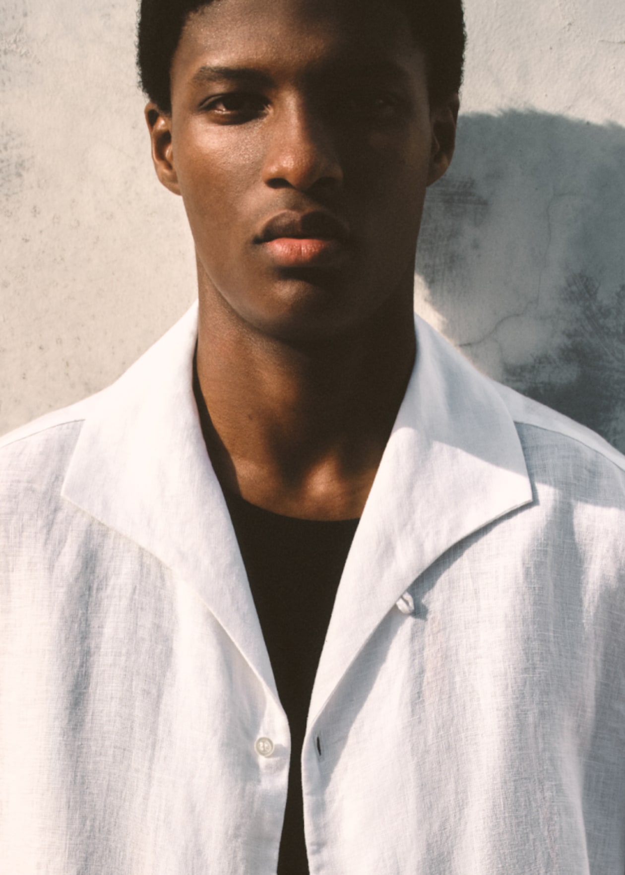 Model wearing a white linen shirt and leaning against the wall.
