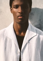 Placeholder for: Model wearing a white linen shirt and leaning against the wall.