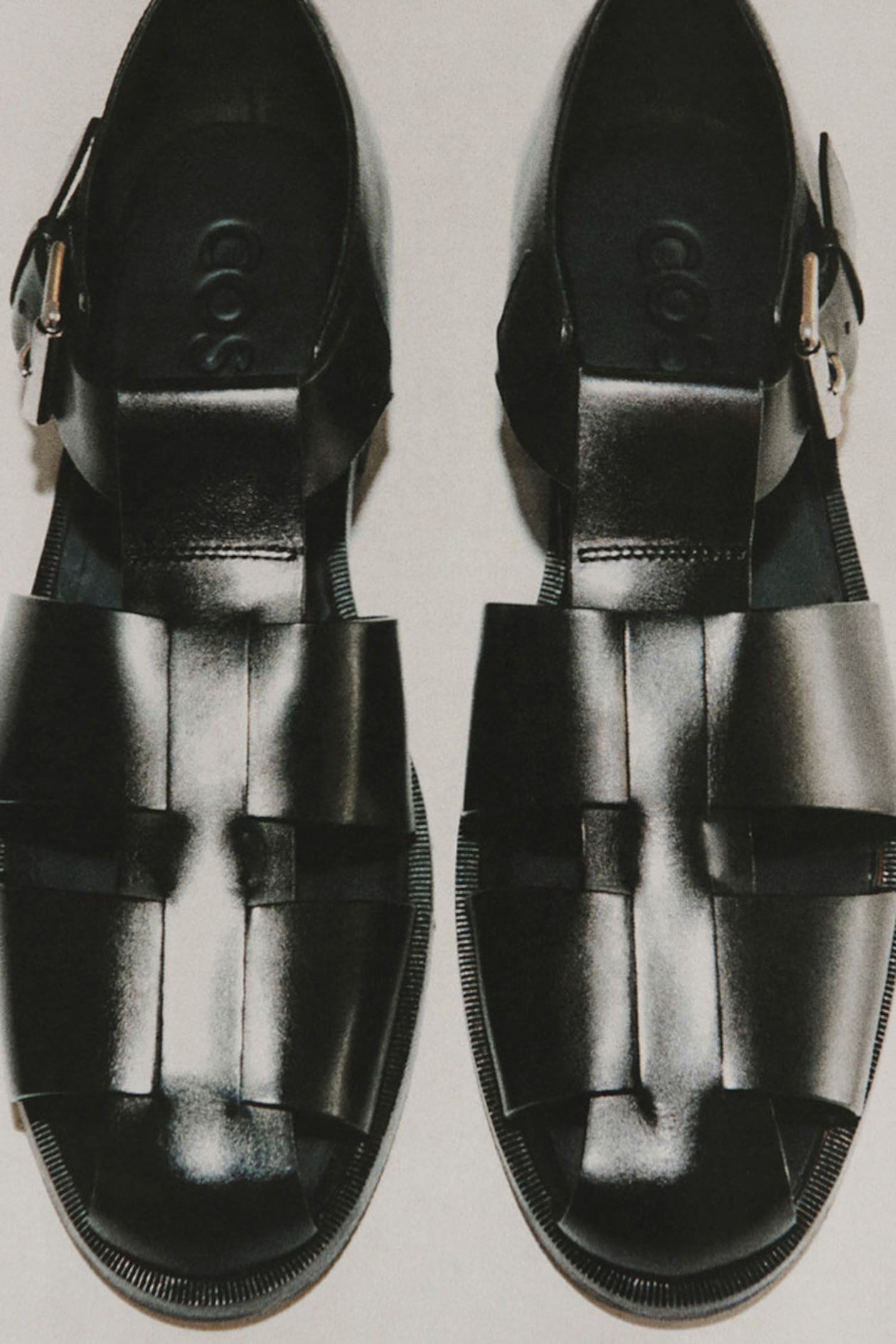 Pair of black leather sandals with woven design and buckles, viewed from above on a light background.