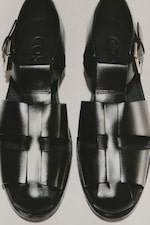 Placeholder for: Pair of black leather sandals with woven design and buckles, viewed from above on a light background.