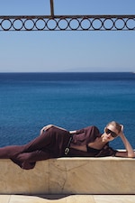 Placeholder for: Person in sunglasses and dark outfit lounging on a marble ledge with a clear blue sea in the background.