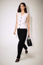 Placeholder for: A woman with long hair wearing a sleeveless beige top and black trousers, carrying a black handbag, walks confidently on a light background.
