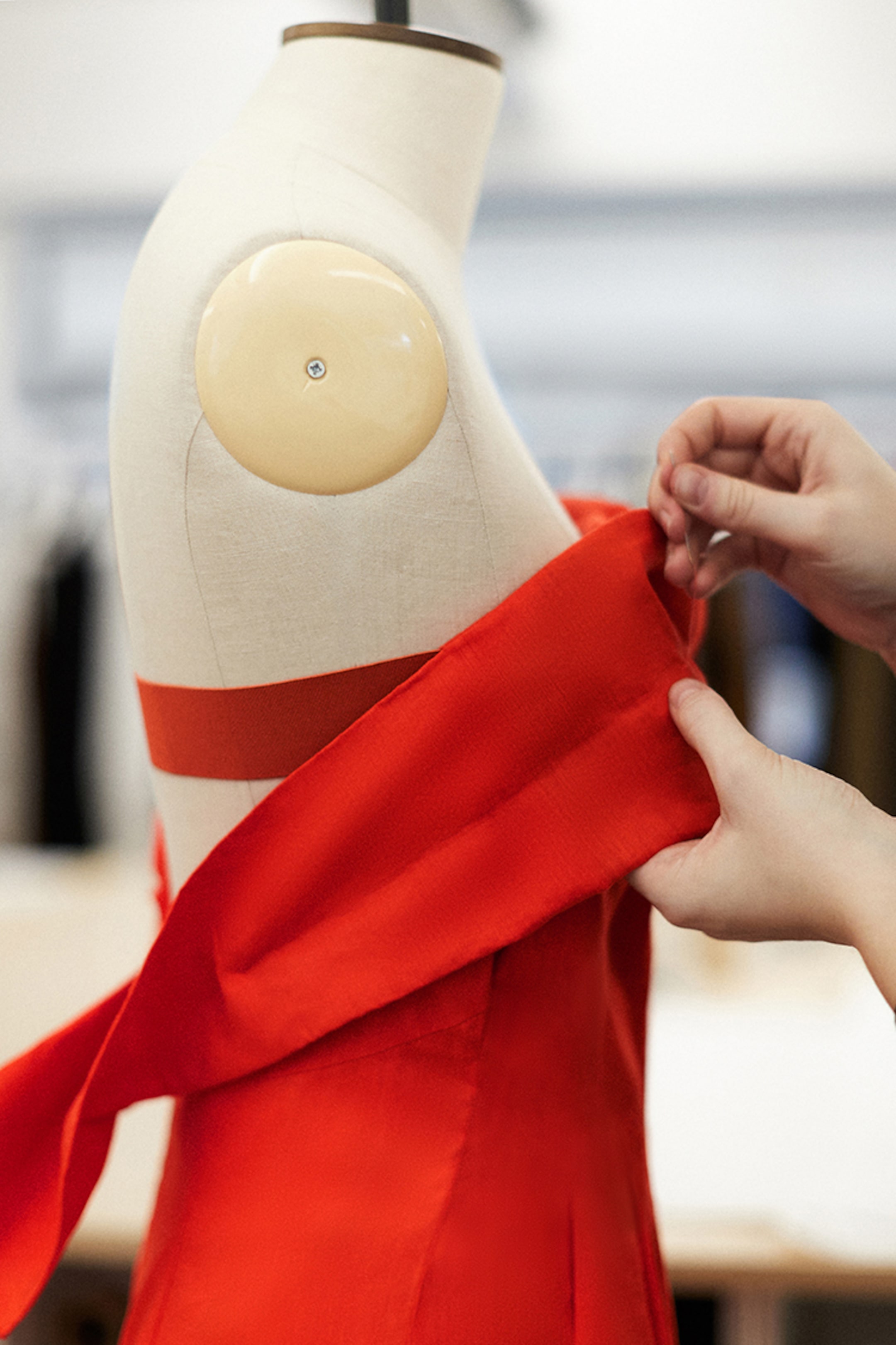 A person drapes vibrant red fabric over a dress form in a fashion studio, preparing to design a garment.