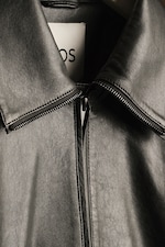 Placeholder for: Close-up of a black leather jacket with a visible zipper and collar, hanging on a hanger. A label is partially visible inside.