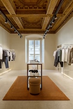 Placeholder for: Clothing store with elegant wooden ceiling, racks of clothes, central display table, and a large window providing natural light.