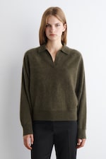 Placeholder for: A person wearing a dark green fuzzy sweater stands against a plain white background, with a neutral expression and straight blonde hair.