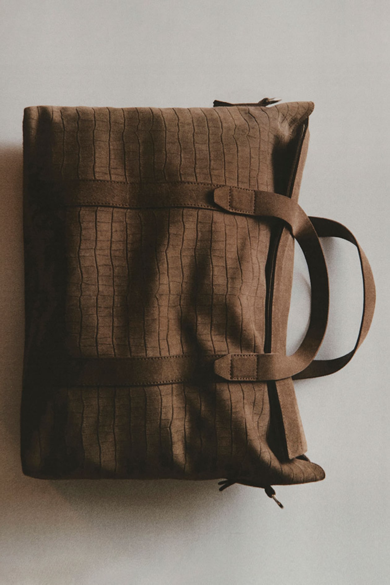 Brown textured duffel bag with two handles, lying flat on a light surface.