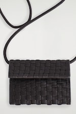 Placeholder for: A black woven leather crossbody bag with a flap closure and adjustable strap, set on a light gray background.