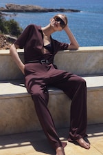 Placeholder for: Woman in a burgundy jumpsuit and sunglasses relaxes on a stone bench by the sea on a sunny day.