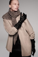 Placeholder for: Person wearing a beige coat, dark gloves, and a brown scarf looking to the side against a neutral background.