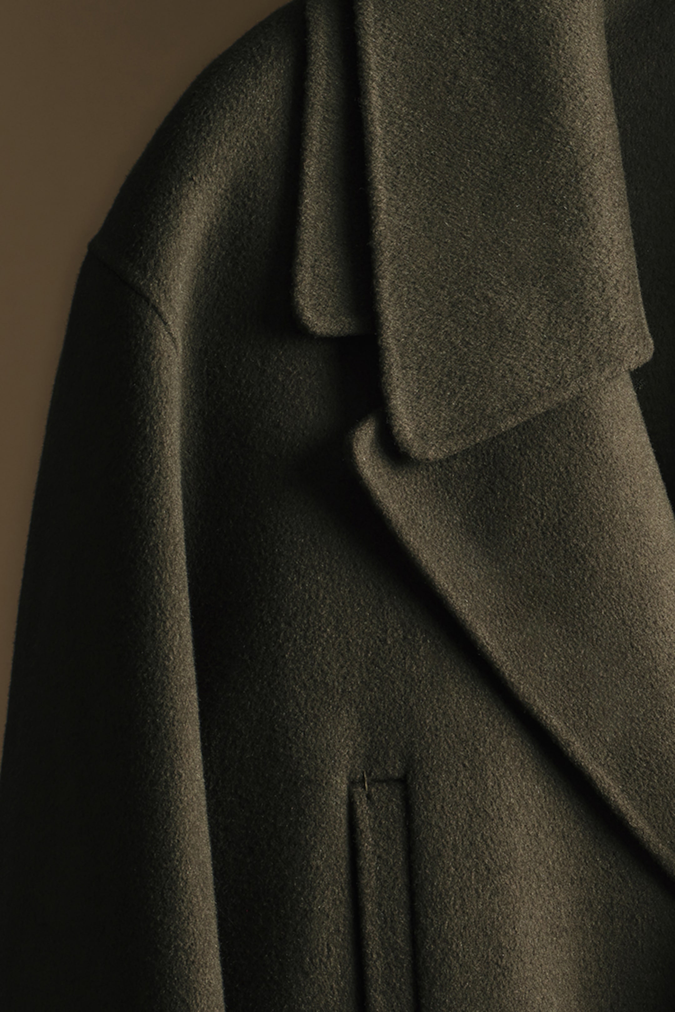 Close-up of a dark brown wool coat with wide lapels and a visible pocket, set against a neutral background.