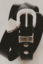 Placeholder for: Close-up of a black leather belt with a silver buckle and rivet details, coiled in a spiral shape on a light background.