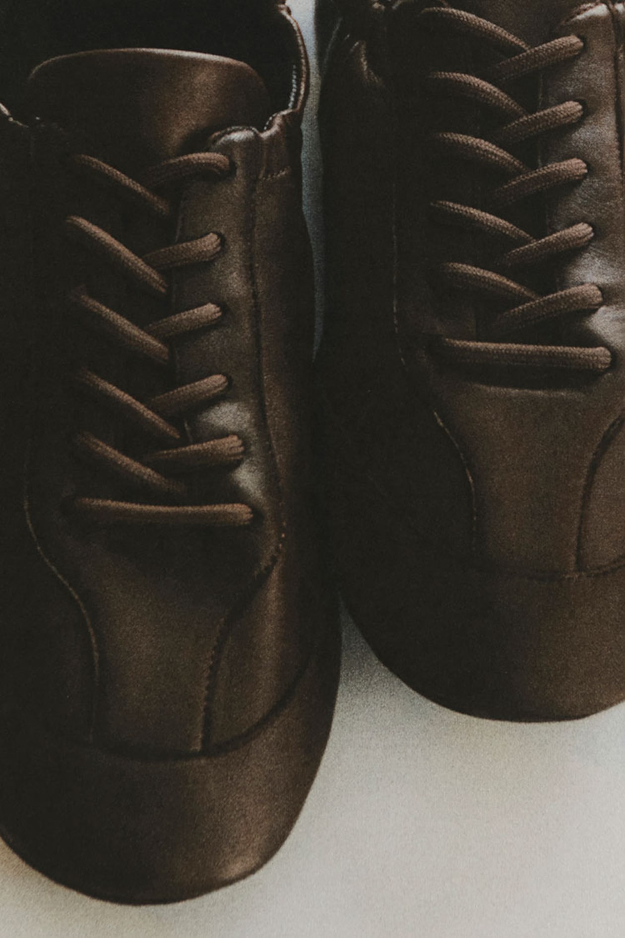 Close-up of a pair of brown leather shoes with dark laces, lying on a light surface.