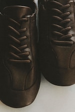 Placeholder for: Close-up of a pair of brown leather shoes with dark laces, lying on a light surface.