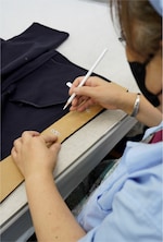 Placeholder for: Person marking fabric with a pencil through a cardboard template, preparing for sewing.