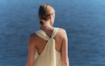 Placeholder for: Woman in a sleeveless dress with a back knot stands overlooking calm blue water.