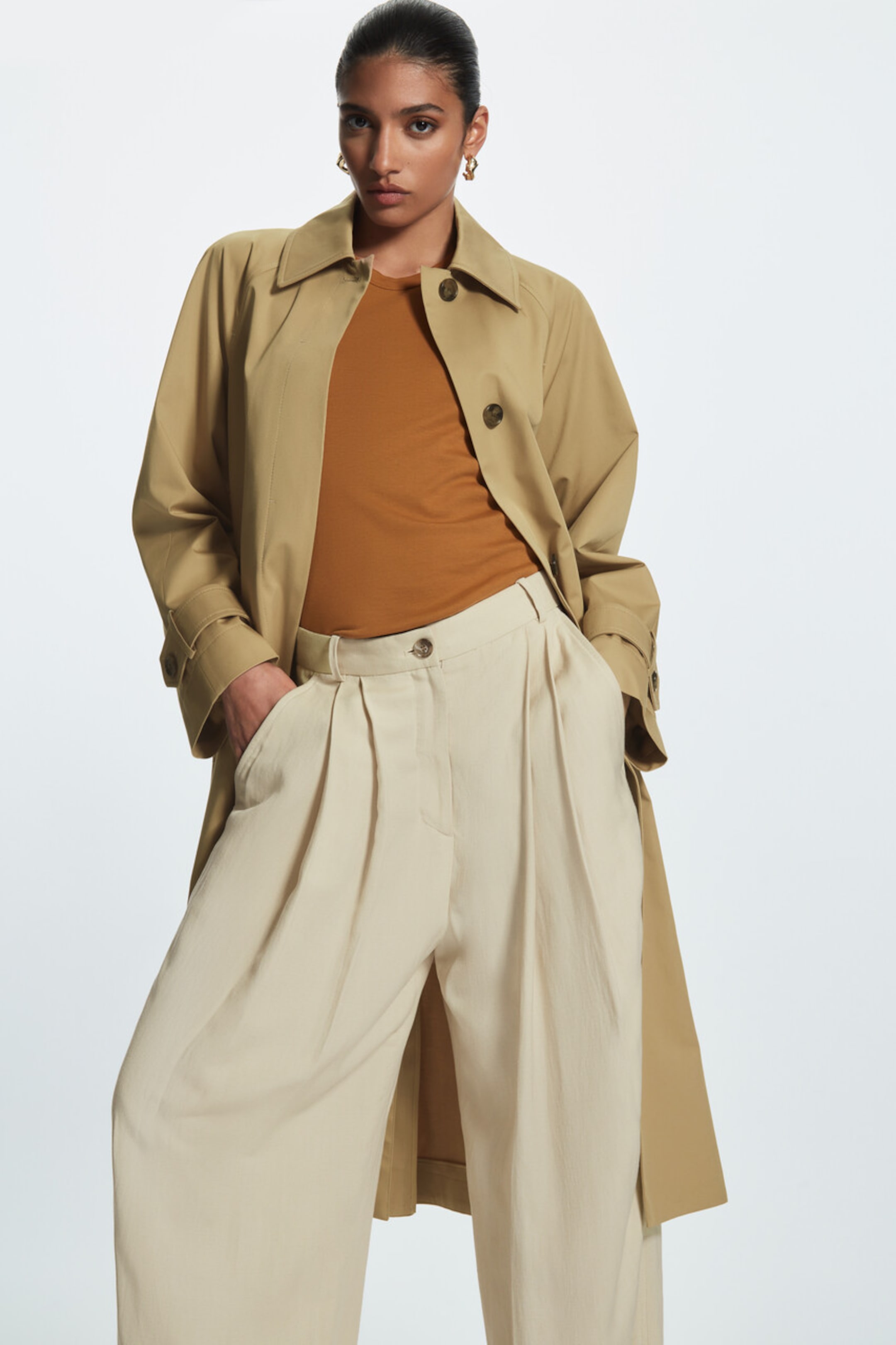 Woman wearing beige trench, orange top and beige tailored trousers