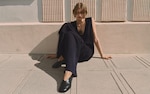 Placeholder for: Woman in black sitting against concrete wall