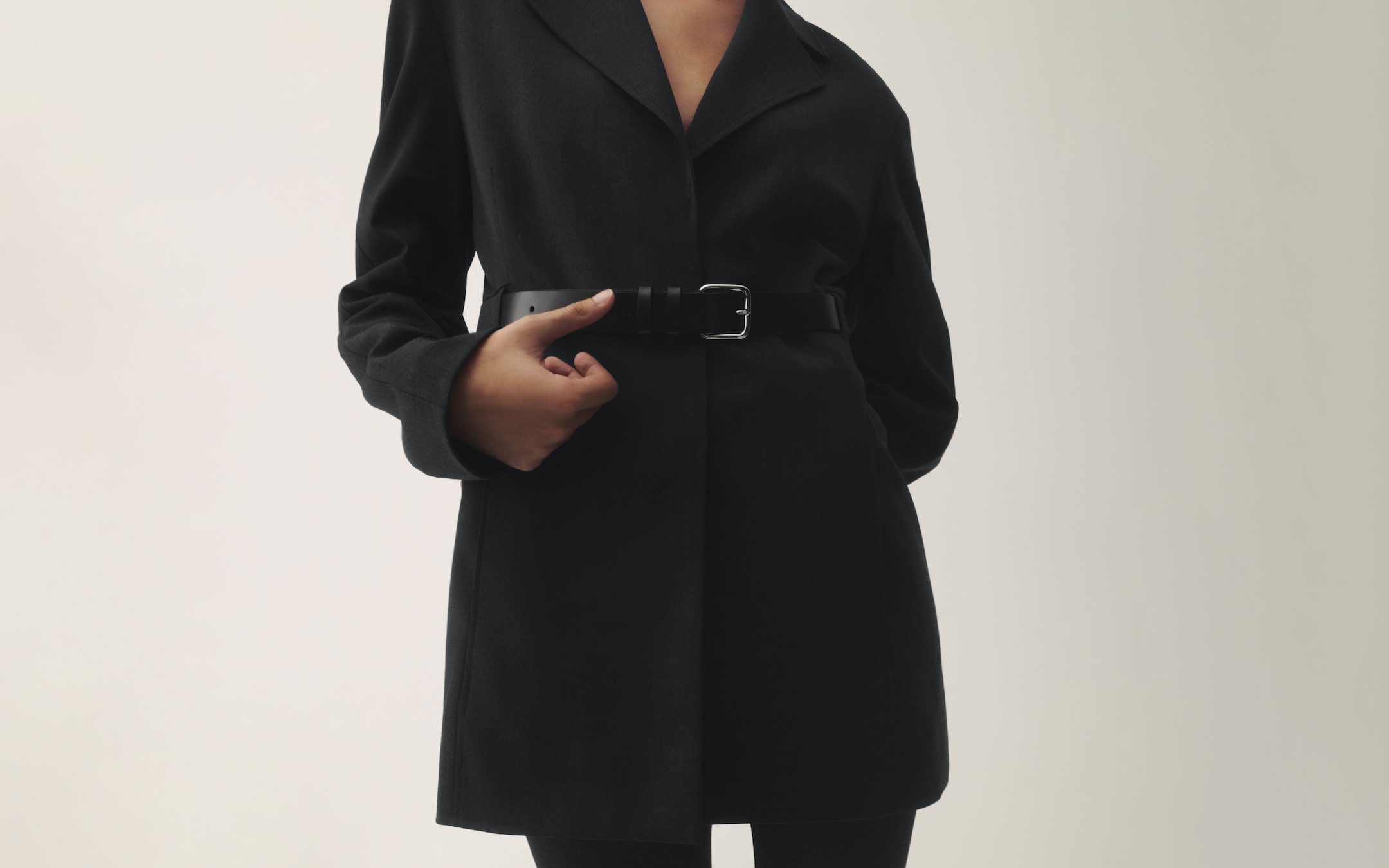 Person wearing a black belted coat, standing against a neutral background.